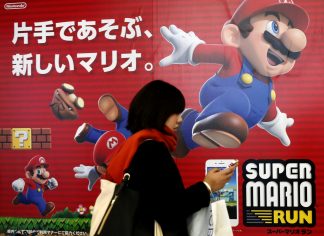A woman using a smartphone walks past Nintendo’s “Super Mario Run” game advertisement board at a subway station in Tokyo, Japan