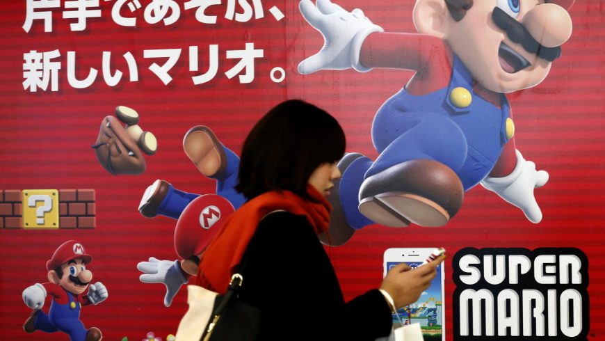A woman using a smartphone walks past Nintendo’s “Super Mario Run” game advertisement board at a subway station in Tokyo, Japan